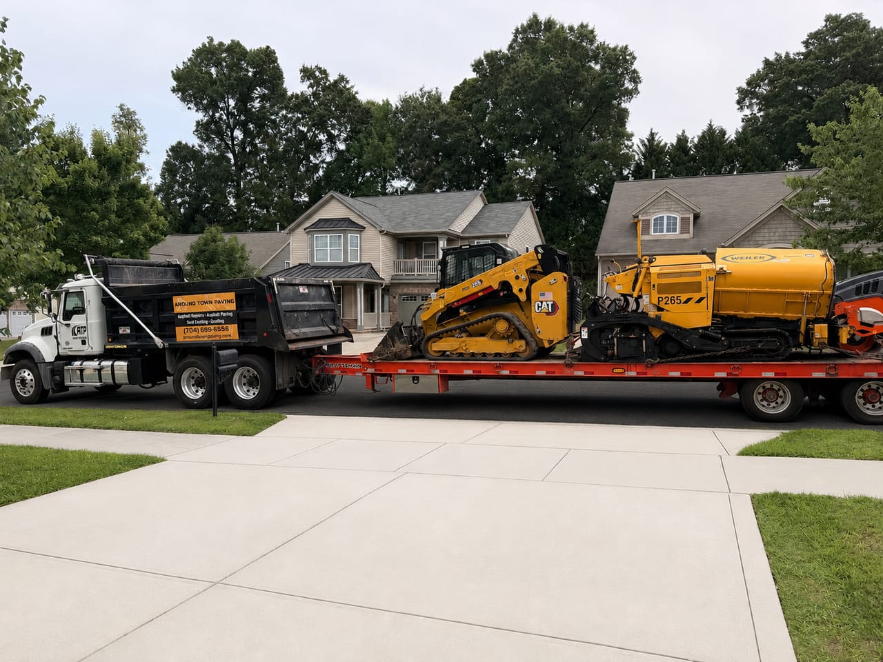 Around Town Paving flatbed trailer loaded with a CAT skid steer loader and a Weiler asphalt paver parked in front of a home in the Concord, NC area