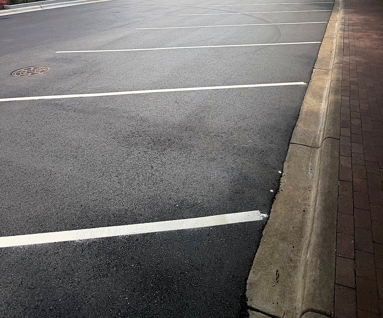 Newly paved downtown parking lot with crisp white striping and brick curb in Kannapolis, NC
